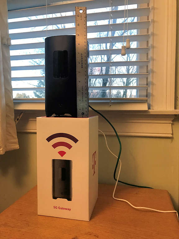 Photo of 5G gateway device standing on its shipping carton in front of a window. The device is nine inches tall.